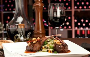 Close up of lamb chops with couscous and vegetables with a sauce of caramel, pepper and spices in a restaurant setting.